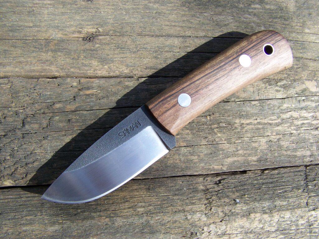 Small Trapper EDC knife with a wooden handle on a brown leather sheath